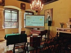 Zdjęcie z sali konferencyjnej, widoczne krzesła, stół prelegenta gotowy do prezentacji oraz rzutnik z wyświetloną prezentacja nt. Polskiej Biblioteki Muzycznej